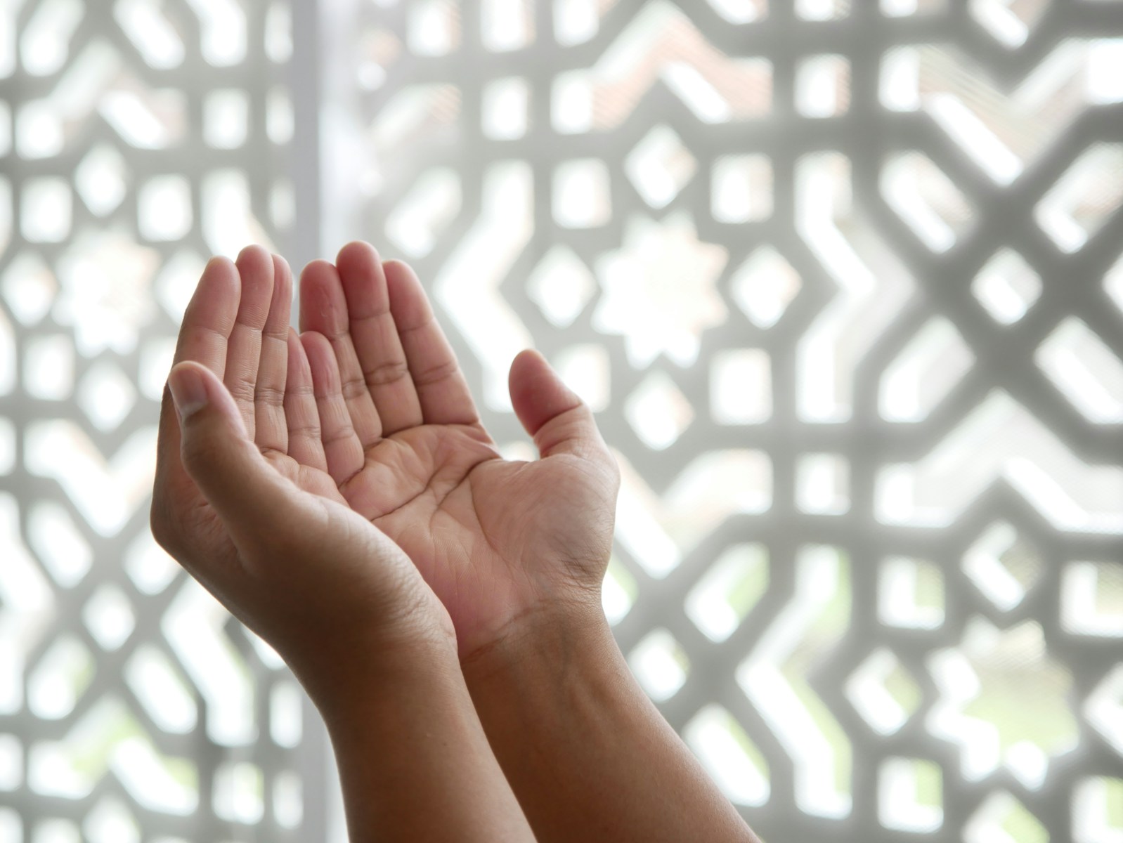 Photo by Masjid MABA a person holding their hands up in front of a window